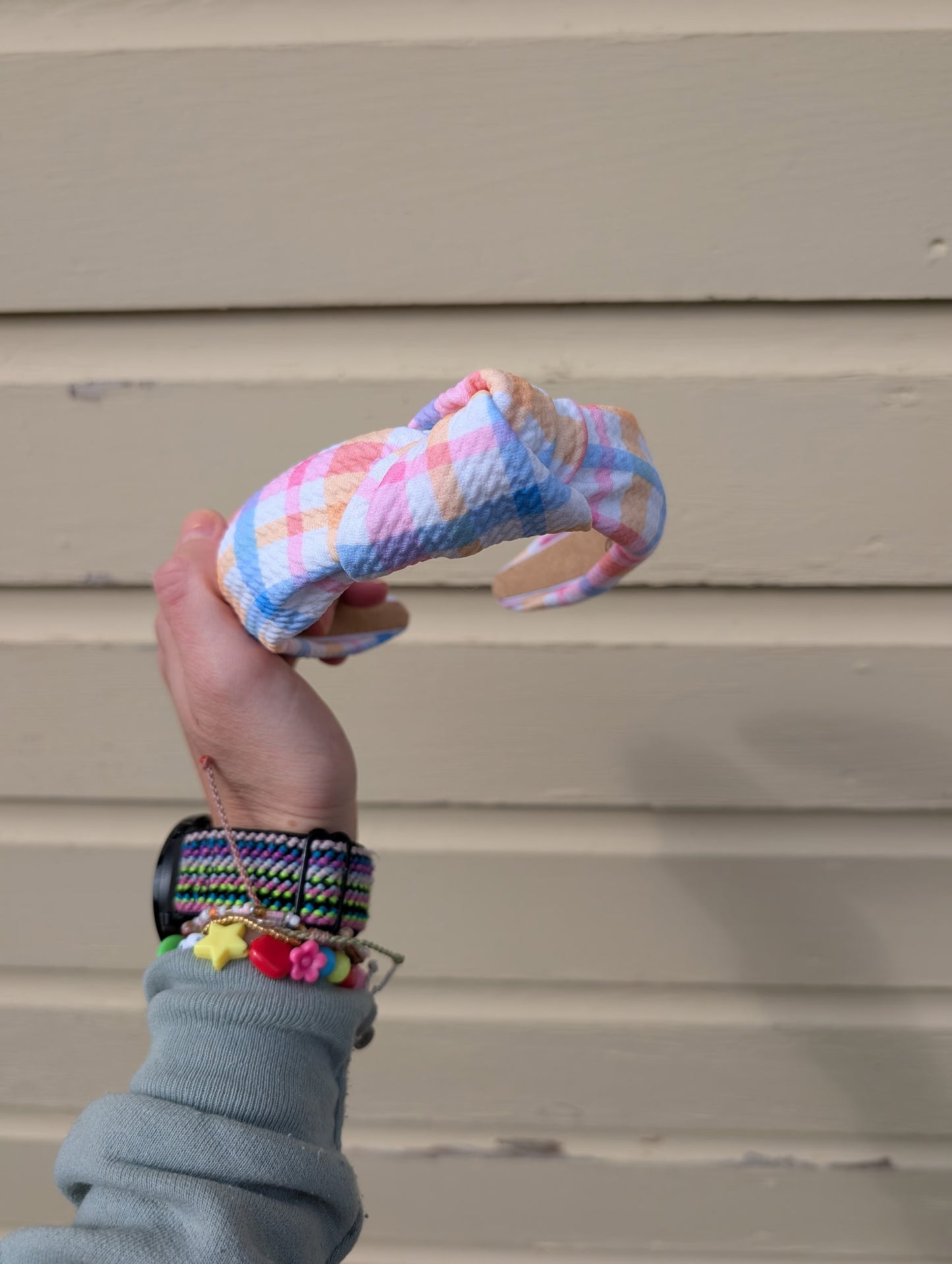Hand holding a colorful knitted item against a beige wall.