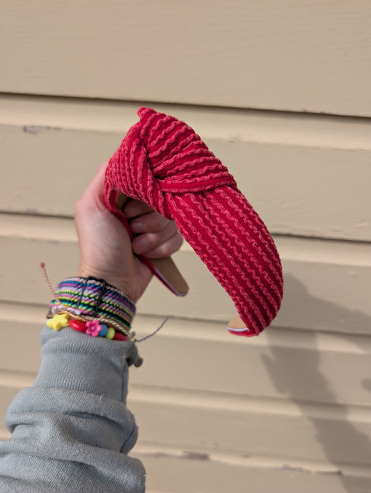 Hand holding a red knotted headband against a beige wall.