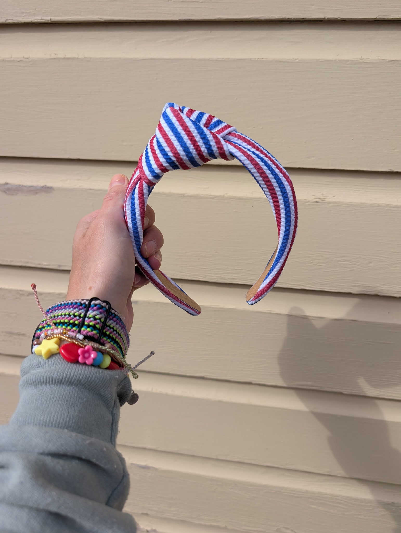Hand holding a colorful blue and red striped headband against a beige wall.