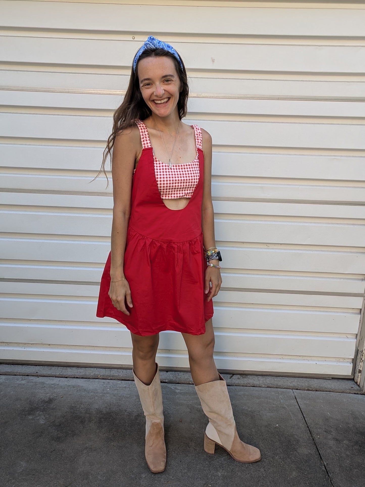 Woman wearing a red dress with a checkered top and beige boots standing in front of a white wall.