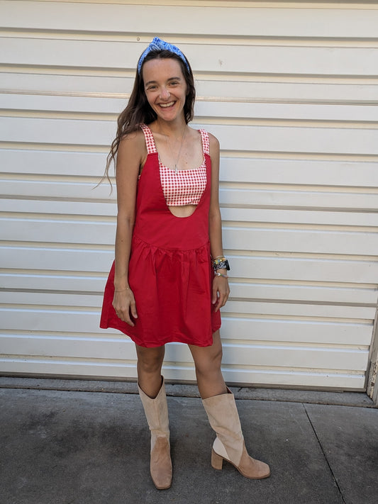 Woman wearing a red dress with a checkered top and beige boots standing in front of a white wall.