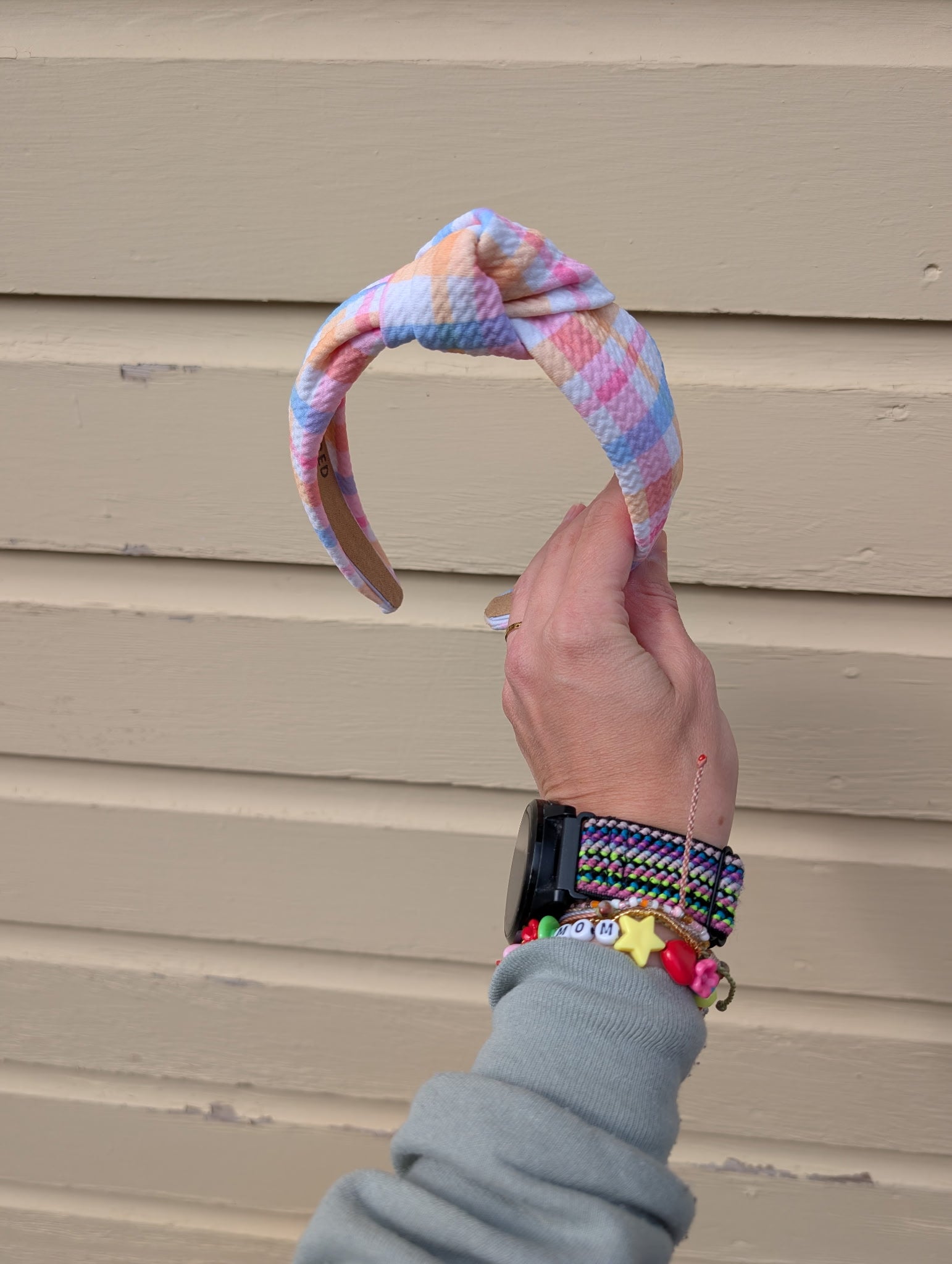 Hand holding a colorful knotted headband against a beige wall.