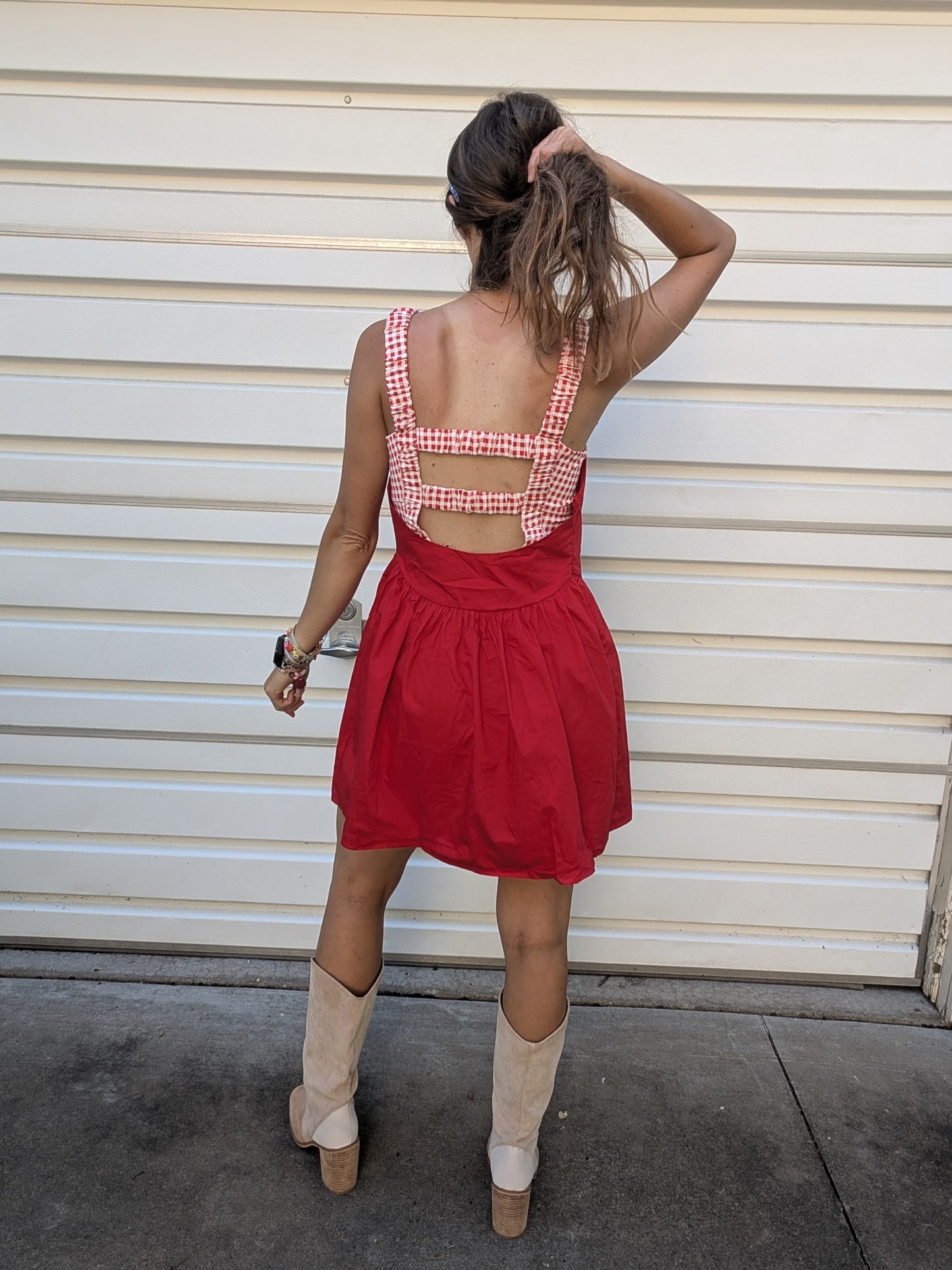 Person wearing a red dress with a checkered top in front of a beige wall.