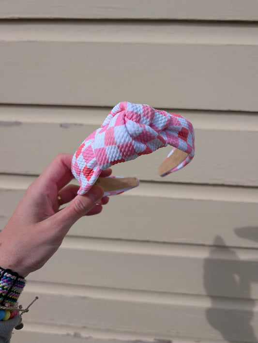 Hand holding a pink and white checkered dog toy against a beige wall.
