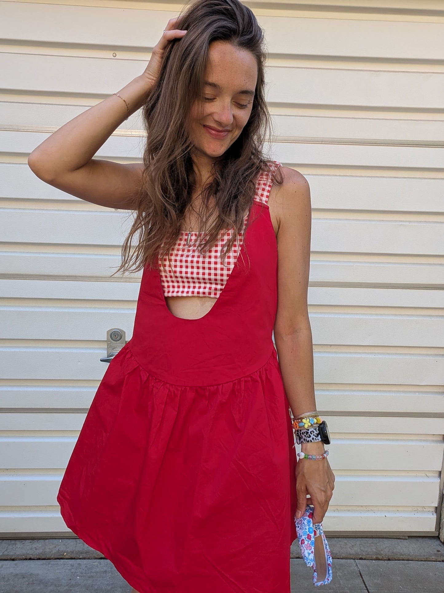 Woman wearing a red dress over a checkered top against a beige wall.