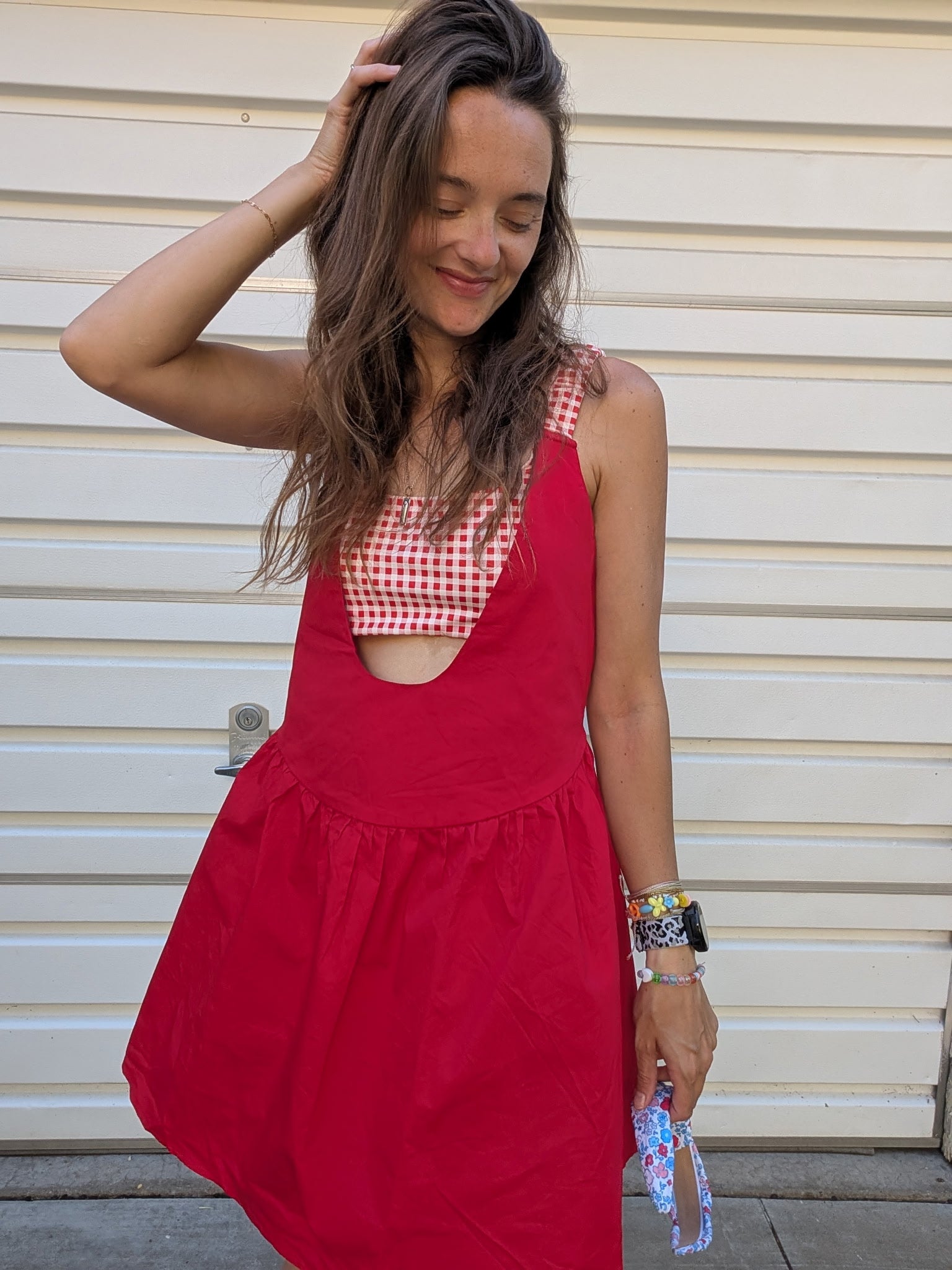 Woman wearing a red dress over a checkered top against a beige wall.
