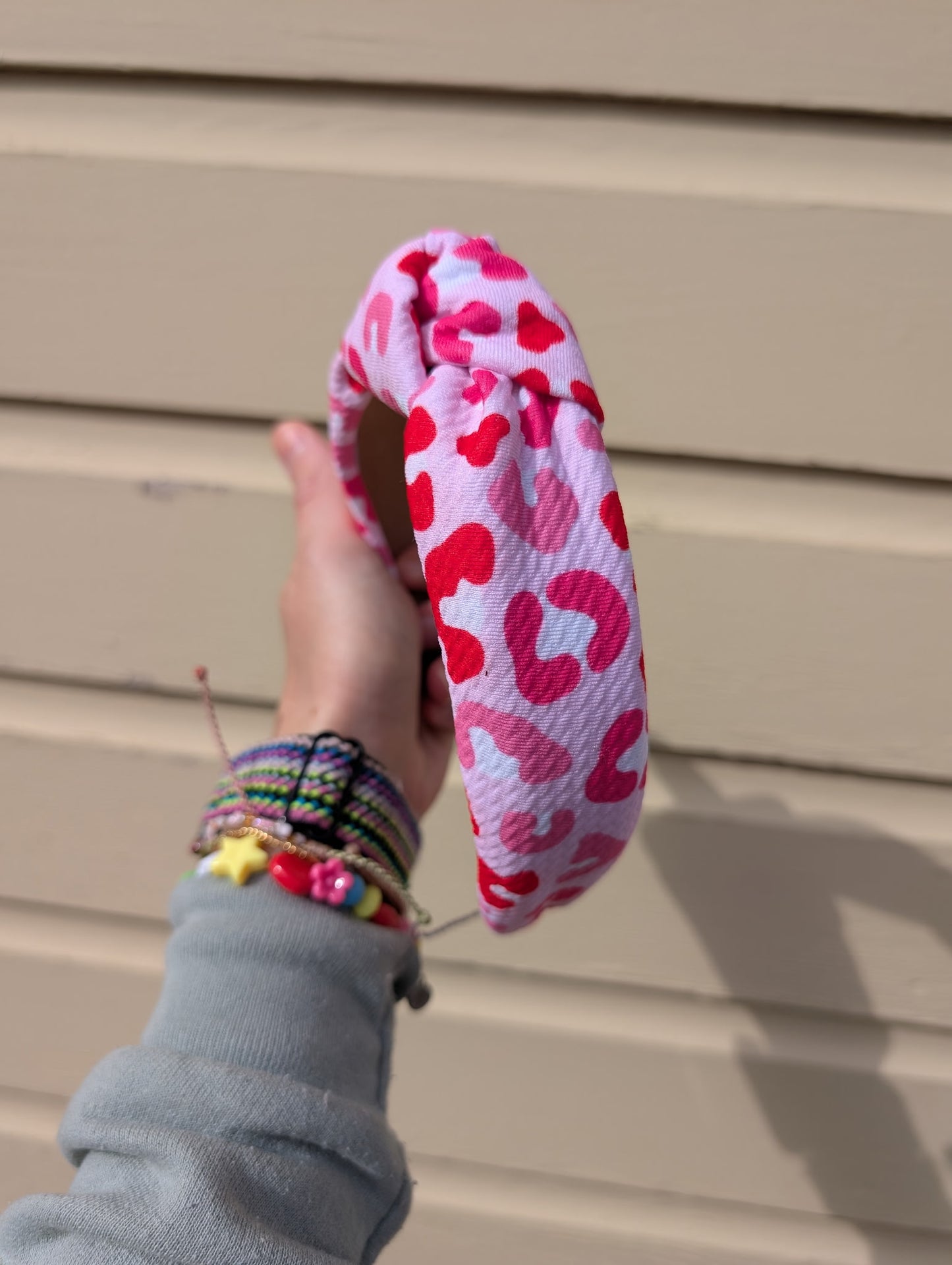 Hand holding a pink and red leopard patterned headband against a beige wall.