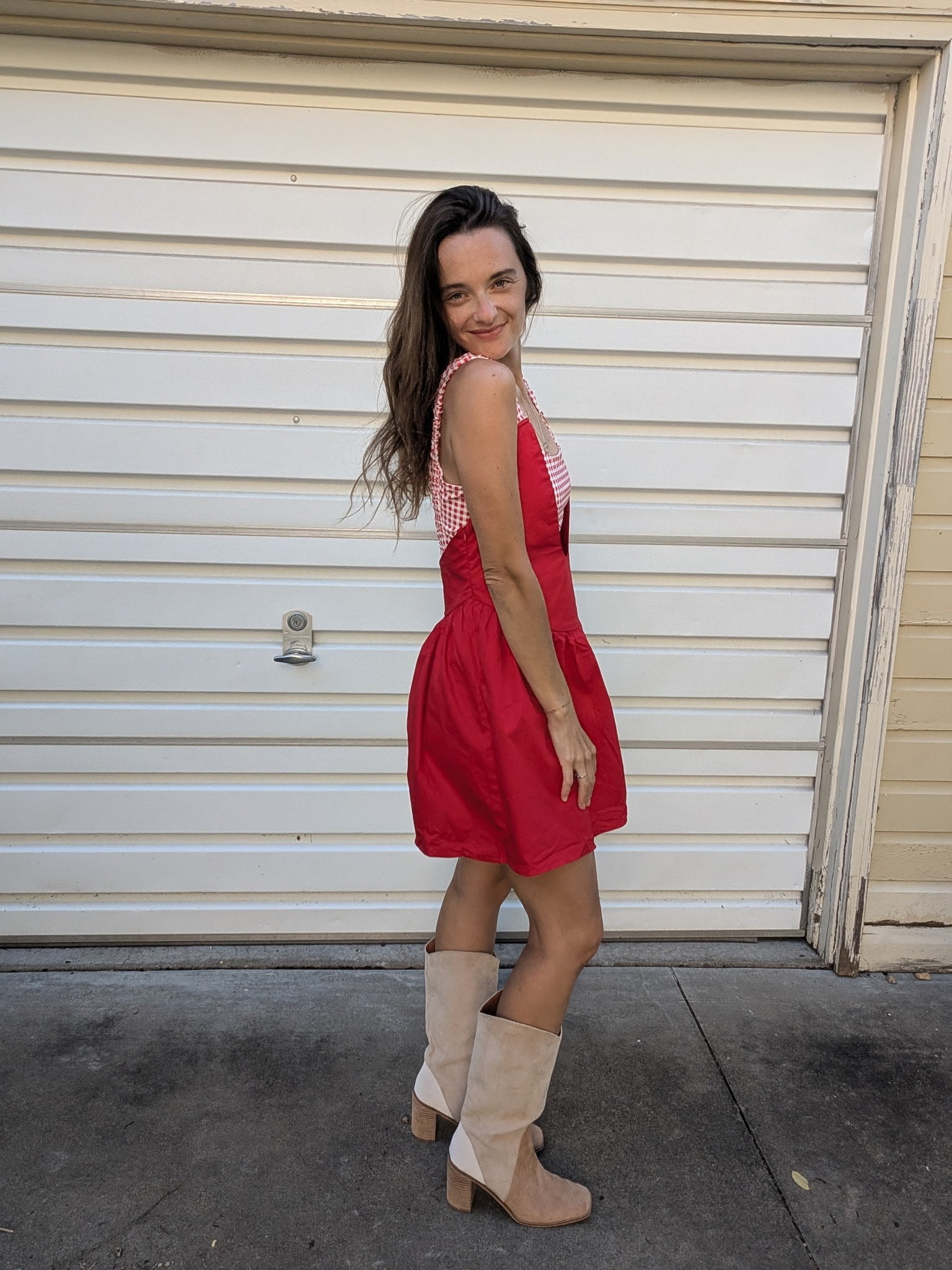 Woman in a red dress and beige boots standing in front of a closed garage door.