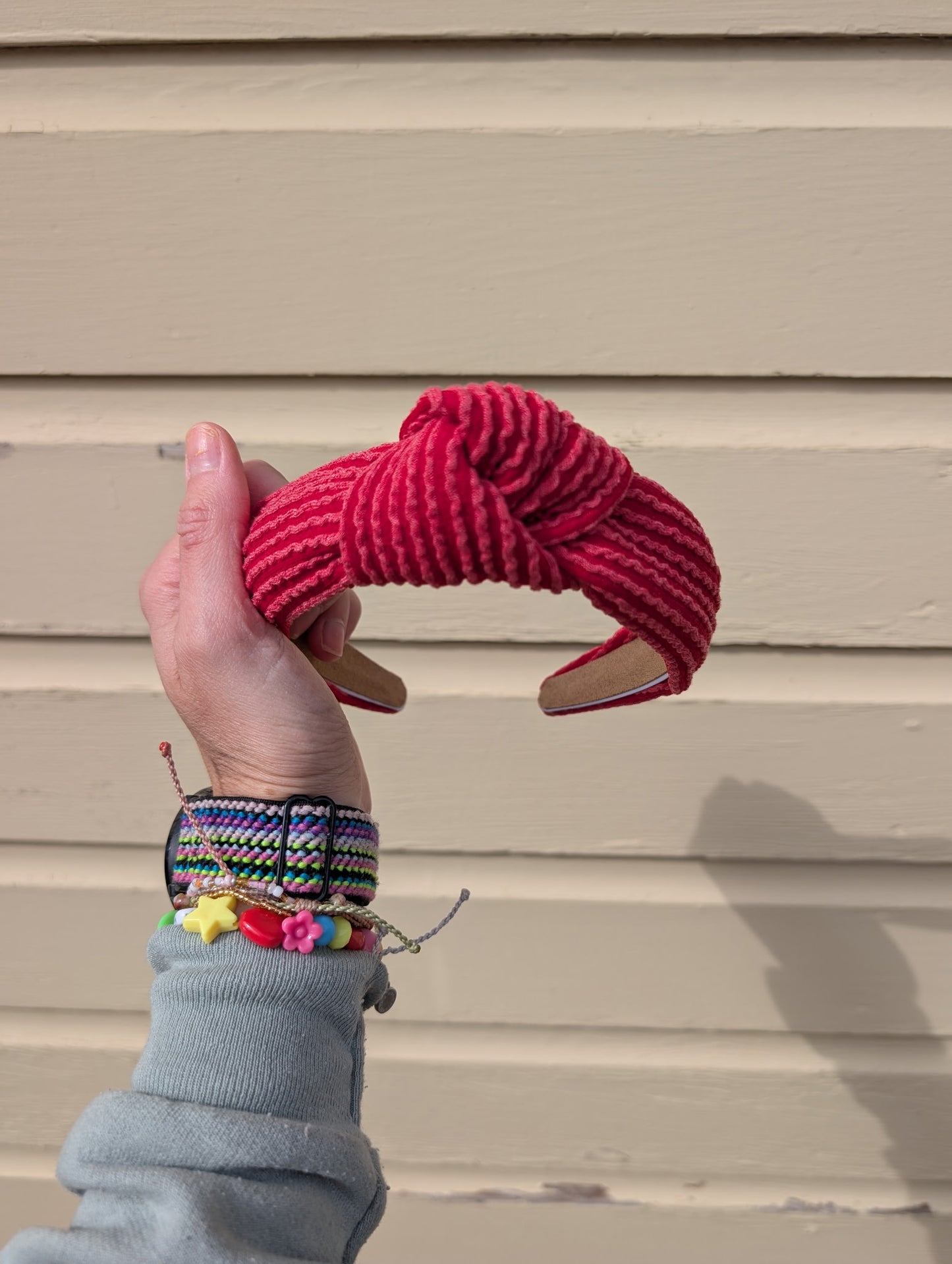 Hand holding a red knotted headband against a beige wall.