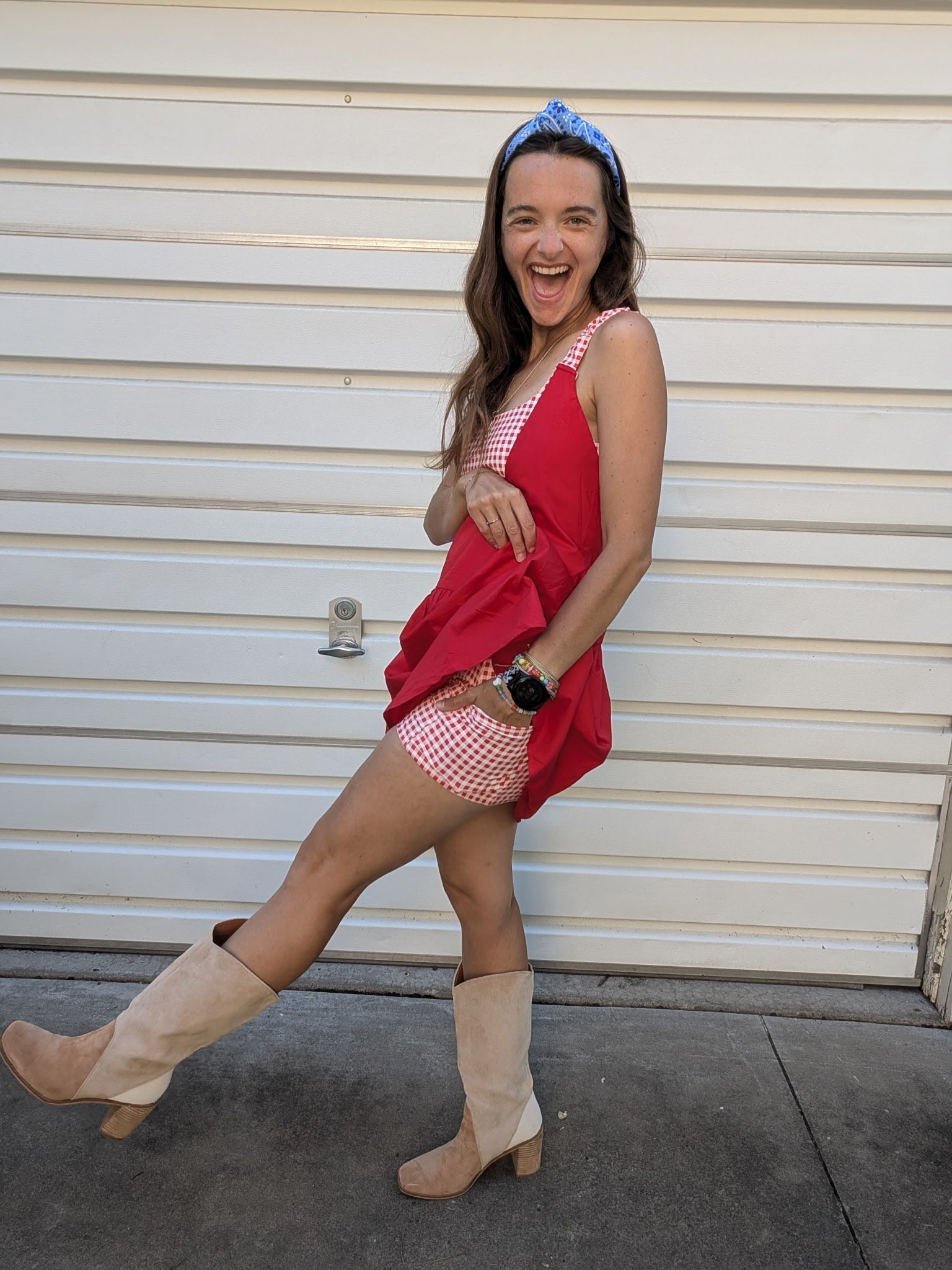 Woman in a red top and checkered shorts with beige boots standing in front of a white garage door.