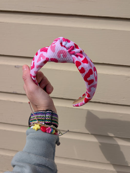 Hand holding a pink and red leopard patterned headband against a beige wall.